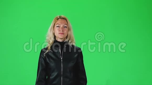 穿着黑色皮夹克的金发女孩在绿色屏幕上直视着相机慢动作视频的预览图