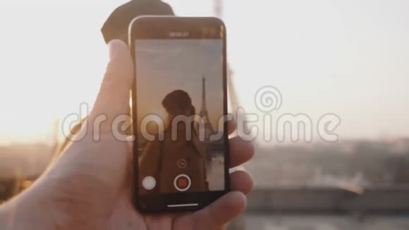 男性手正在制作智能手机视频快乐微笑的女人在日落埃菲尔铁塔附近的度假慢动作视频的预览图