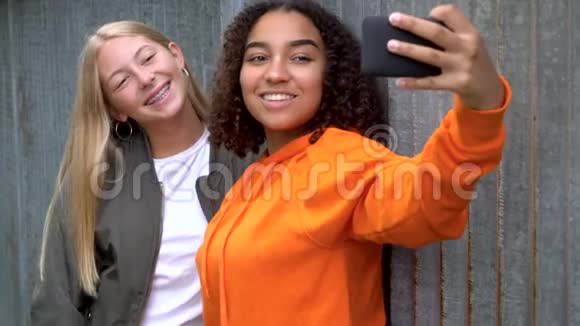 漂亮的金发女孩和混血的青少年女性在社交媒体上的智能手机上自拍视频的预览图