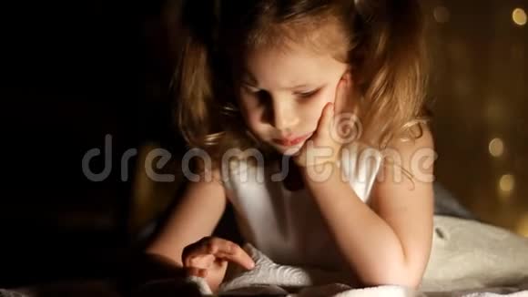 小女孩躺在床上在黑暗中玩智能手机孩子的近脸被明亮的灯光照亮视频的预览图