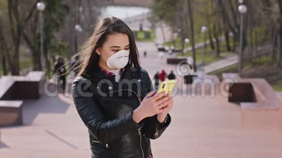 有魅力的年轻女性戴着防护面罩站在楼梯上的摄像机前用手机视频的预览图