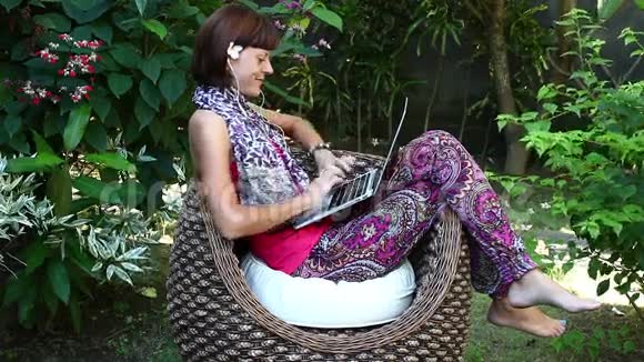 美丽的自由职业者妇女在她的别墅与绿色热带花园在电脑上工作印度尼西亚巴厘岛视频的预览图