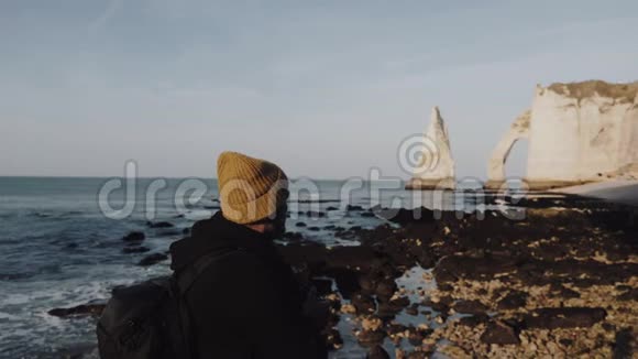 微笑的男性游客用相机观看史诗般的自然景观在阳光下的洛基诺曼底海滩和海边悬崖缓慢的运动视频的预览图