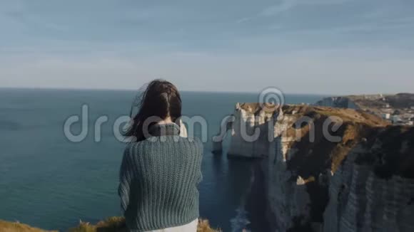 背景拍摄兴奋的女游客观看华丽的Etretat岩石和海洋全景与头发在风中吹起视频的预览图