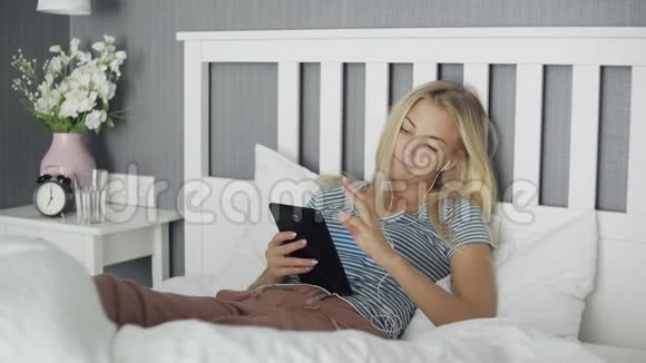 躺在家里的床上躺在平板电脑里浏览社交媒体的无聊青年女子视频的预览图