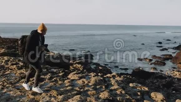 快乐的男摄影师踩着岩石海滩拍着令人叹为观止的阳光灿烂的诺曼底海岸悬崖的慢动作视频的预览图