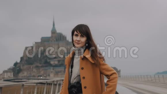 美丽的平静的深色头发的摄影师在神奇的圣米歇尔山城堡慢镜头前微笑的女人的肖像视频的预览图