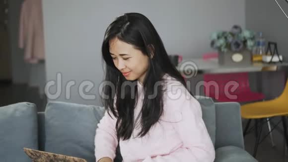 积极的女孩从家里远程工作笔记本电脑喝咖啡坐在沙发上视频的预览图
