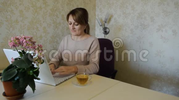 这个女人在笔记本上做笔记在家里在电脑上工作而不离开家视频的预览图