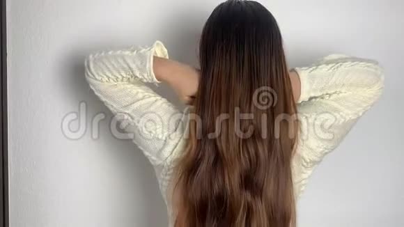 穿着白色连衣裙的欧洲年轻女孩在家里梳着她天然的长发挺直了头发发型护理理念视频的预览图