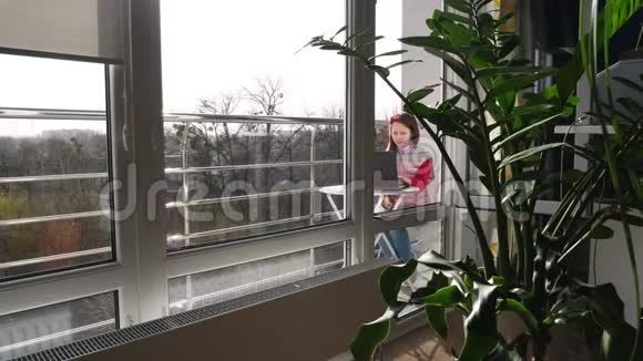 漂亮的少女正在打字在笔记本电脑上工作在开放的阳台上春天阳光明媚的一天远程学习概念视频的预览图