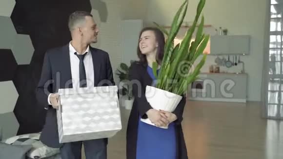 快乐的一对夫妇带着东西和花在新公寓里年轻人微笑拥抱视频的预览图