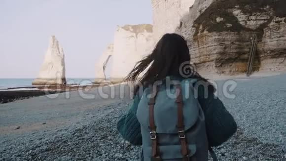 镜头跟随快乐的旅游妇女与bckpack探索白色阳光Etretat岩石在诺曼底海岸慢动作视频的预览图