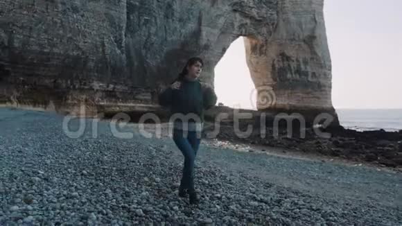 美丽快乐的黑发旅游妇女与相机和背包探索白色拱形海岩附近的Etretat慢动作视频的预览图