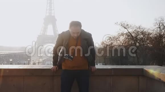 快乐男欧洲自由摄影师男子坐在篱笆上微笑着看埃菲尔铁塔在巴黎慢镜头视频的预览图