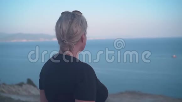后景金发女人站着看着大海女人面前是海山全景视频的预览图