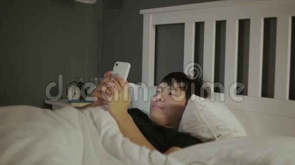 年轻的亚裔男子使用智能手机躺在家里深夜视频的预览图