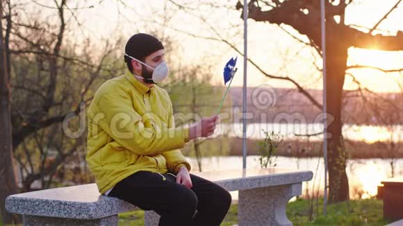 日落时分公园里的年轻人坐在椅子上戴着防护面具玩着一个旋转风的科维德视频的预览图