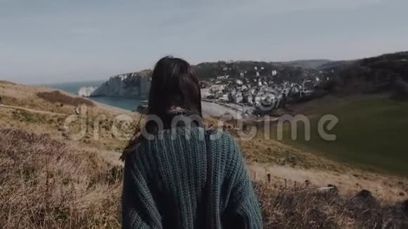 后景美丽的女游客走下山靠近华丽的Etretat海岩黑发在风中吹起视频的预览图
