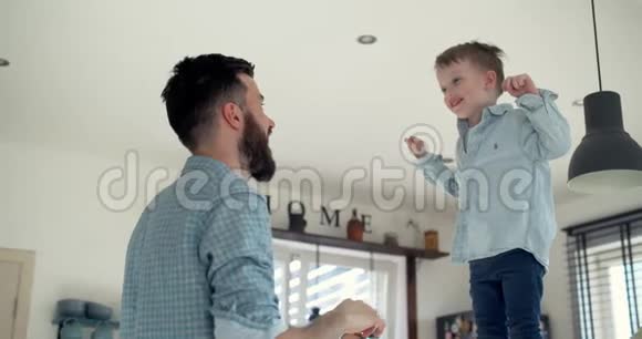 快乐年轻的欧洲父亲和快乐的小儿子一起玩在他的怀里跳着现代的房子厨房慢动作视频的预览图