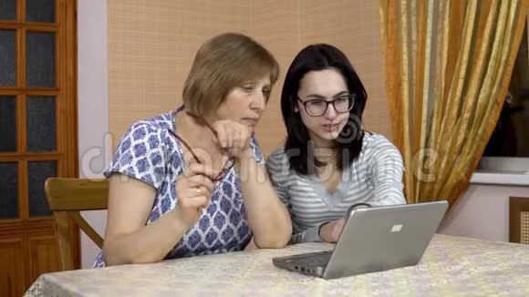 女儿教妈妈如何使用笔记本电脑一个年轻的女人告诉她的老母亲在哪里点击电脑家庭视频的预览图