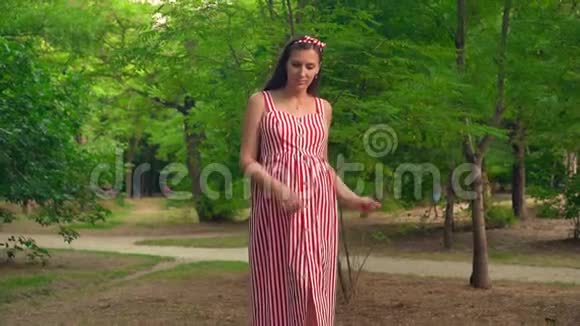 一个怀孕的女孩穿过公园一个穿着条纹白色和红色连衣裙的女孩微笑着跳舞视频的预览图
