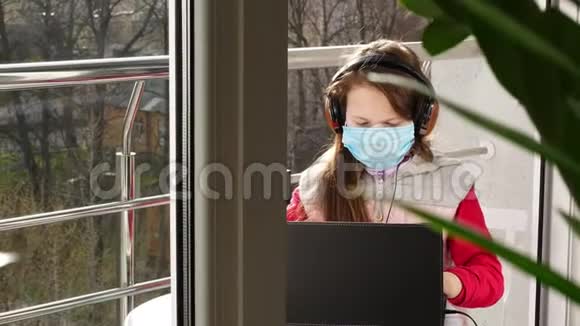 十几岁的女孩戴着面具和耳机打字在笔记本电脑上工作在开放的阳台上春天阳光明媚的一天远程学习视频的预览图