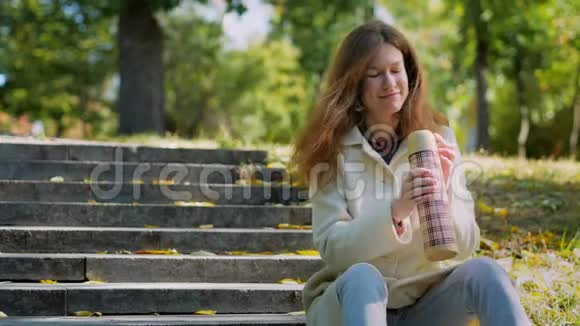 美丽的女人享受秋天公园喝热茶视频的预览图