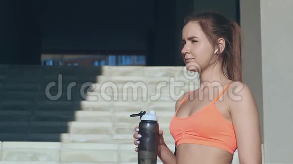 运动的女孩在锻炼后喝水在脸上泼水视频的预览图
