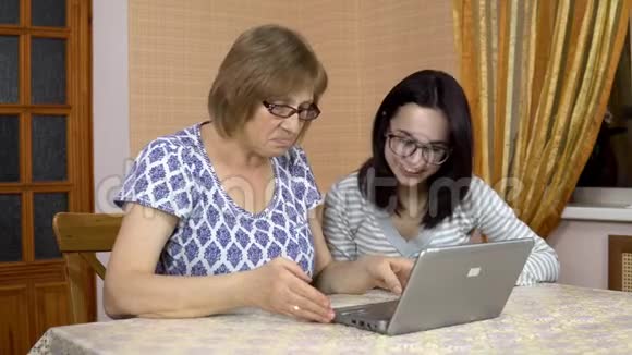女儿教妈妈如何使用笔记本电脑一个年轻的女人告诉她的老母亲在哪里点击电脑家庭视频的预览图