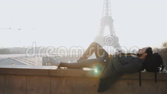 放松的快乐男性游客躺下来闭着眼睛在惊人的日落埃菲尔铁塔观景巴黎慢动作视频的预览图