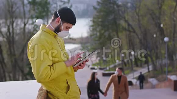 在公园的中央一个戴着防护面罩的家伙呆在他的平板电脑上而另一对夫妇在他们身边走来走去他们有一个视频的预览图