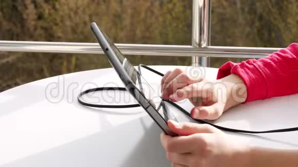 特写双手少年女孩打字在平板电脑上工作在开放的阳台上春天阳光明媚的一天视频的预览图