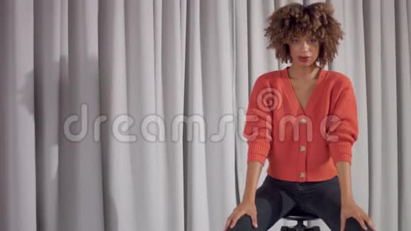 灰色窗帘背景的混血女人坐在椅子上对着镜头摆姿势视频的预览图