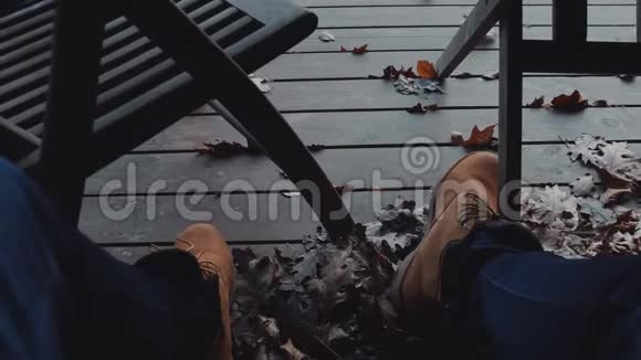 波夫倾斜向上的镜头放松的人坐在秋天的露台上穿着棕色的皮靴在他的房子院子里慢动作视频的预览图