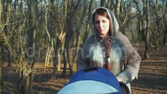 秋天的森林里一个穿着夹克的沉思的女人带着婴儿车在公园里散步一个女人被什么东西迷惑翻滚着视频的预览图