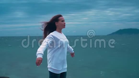 一个女孩在暴风雨中站在海滨多云的一天大海在暴风雨中一个女孩在海滨举手视频的预览图