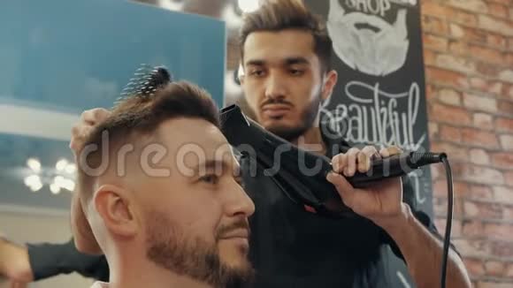 带吹风机的专注理发师为客户烘干头发视频的预览图