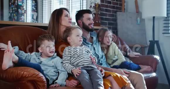 快乐的年轻白种人母亲父亲和三个孩子微笑着在家看电视一起躺在沙发上动作视频的预览图