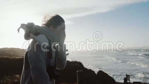 美丽的快乐旅游妇女带着相机站在极冷的风下覆盖着冬天的海面海岸缓慢地视频的预览图
