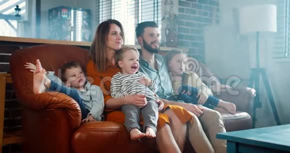 幸福家庭的肖像年轻的白种人父母和三个可爱的孩子在家看有趣的卡通片慢动作视频的预览图