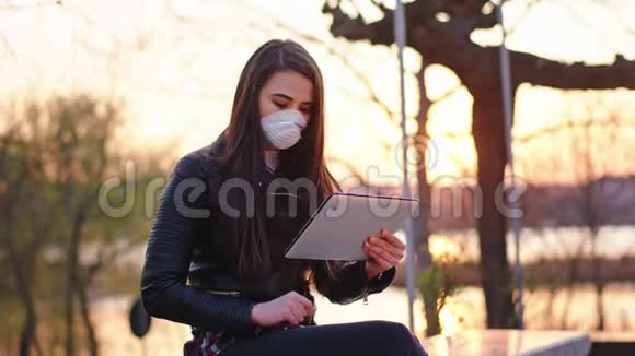 有魅力的女人独自在公园里坐下来她戴着防护面罩在平板电脑上工作以确保安全视频的预览图