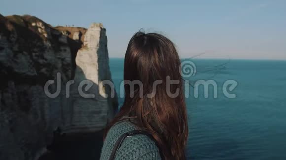 后景快乐的黑发旅游妇女在埃特雷特海岸观看史诗般的风景头发在风中缓慢的运动视频的预览图