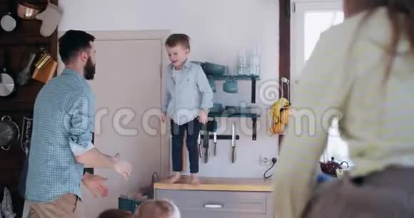 快乐的年轻白种人父亲抓住快乐的小儿子跳在他的怀里家庭娱乐时间在厨房慢动作视频的预览图