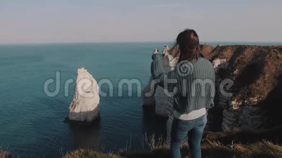 后景开心兴奋的旅游女人看着眼前的Etretat岩石摸着头发在风中缓慢的运动视频的预览图