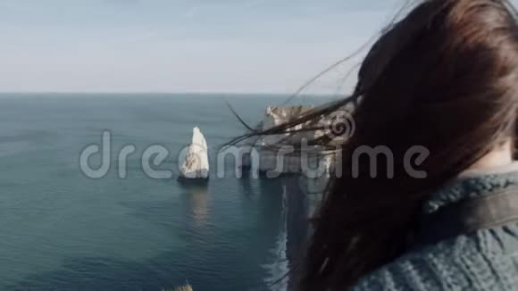 特写年轻的黑发旅游妇女头发随风飘动看着史诗般的埃特雷特岩石海岸缓慢的运动视频的预览图