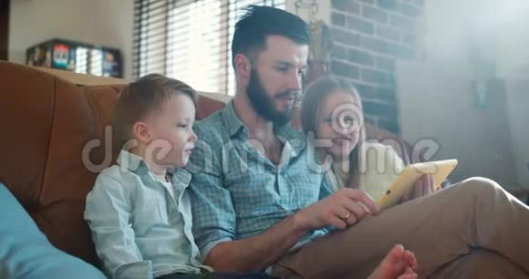 年轻快乐的白种人单身爸爸用平板电脑和可爱的小儿子和女儿一起在家慢动作视频的预览图
