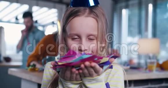 快乐漂亮的810岁白人女孩吹着纸屑看着相机在有趣的生日聚会慢动作视频的预览图