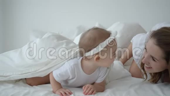 在床上和妈妈躲起来寻找可爱的婴儿女孩视频的预览图