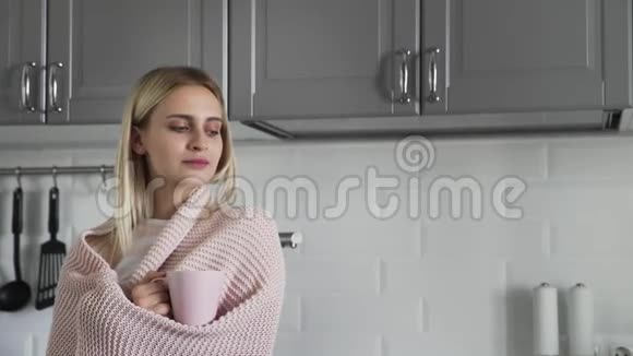 穿着格子毯子的可爱女孩喝茶早上看着厨房的窗外视频的预览图